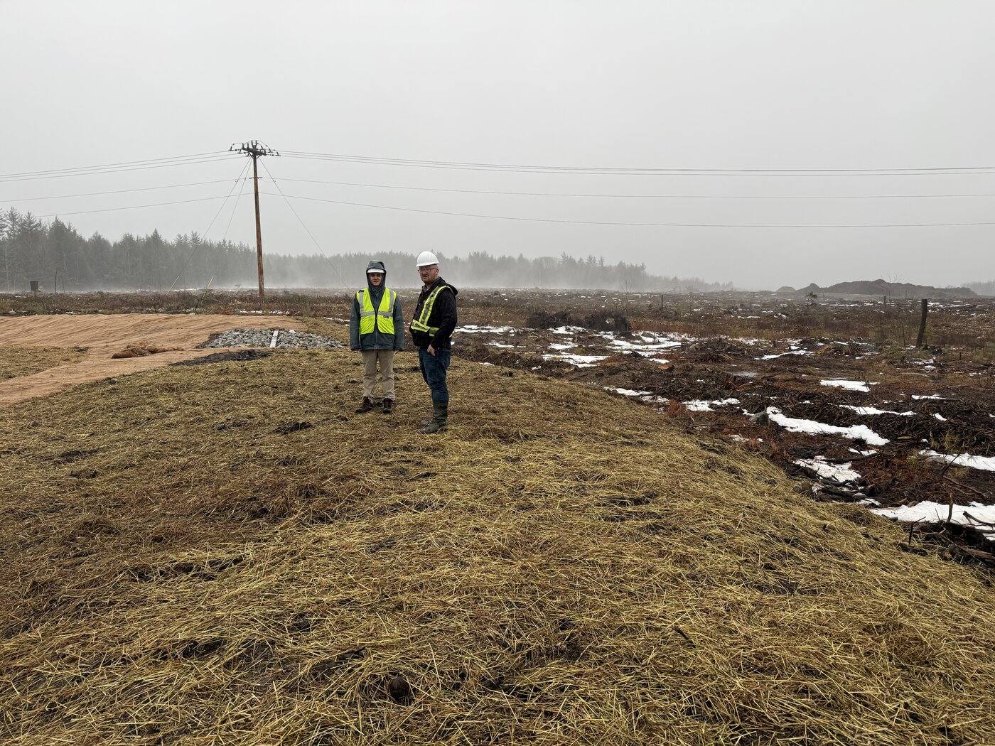 Two EcoLink staff in hard hats reviewing a cleared development site beside a stream