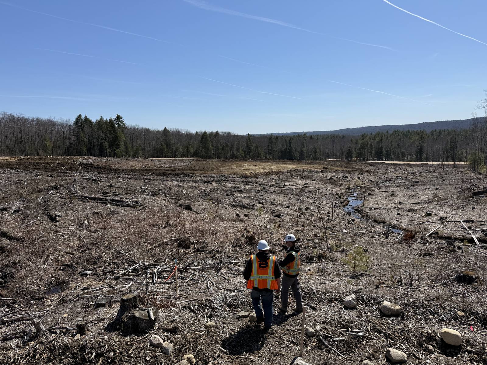 Two inspectors in safety vests surveying a large cleared site in Maine